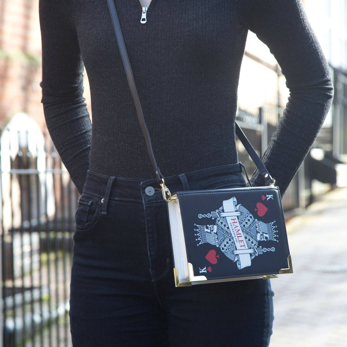 Person wearing a black outfit with a decorative handbag featuring playing card designs.