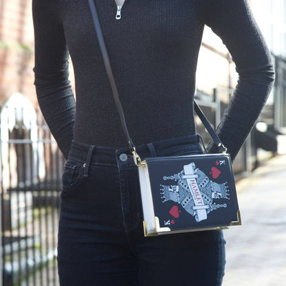 Person wearing a black outfit with a decorative handbag featuring playing card designs.