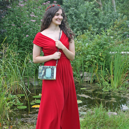Woman in a red dress holding a patterned handbag in a garden setting