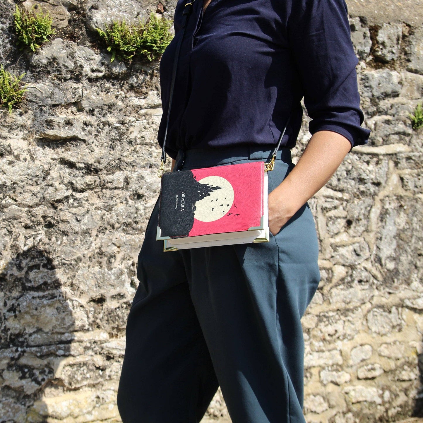 Person holding a book with a red cover against a stone wall