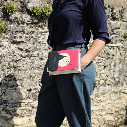 Person holding a book with a red cover against a stone wall
