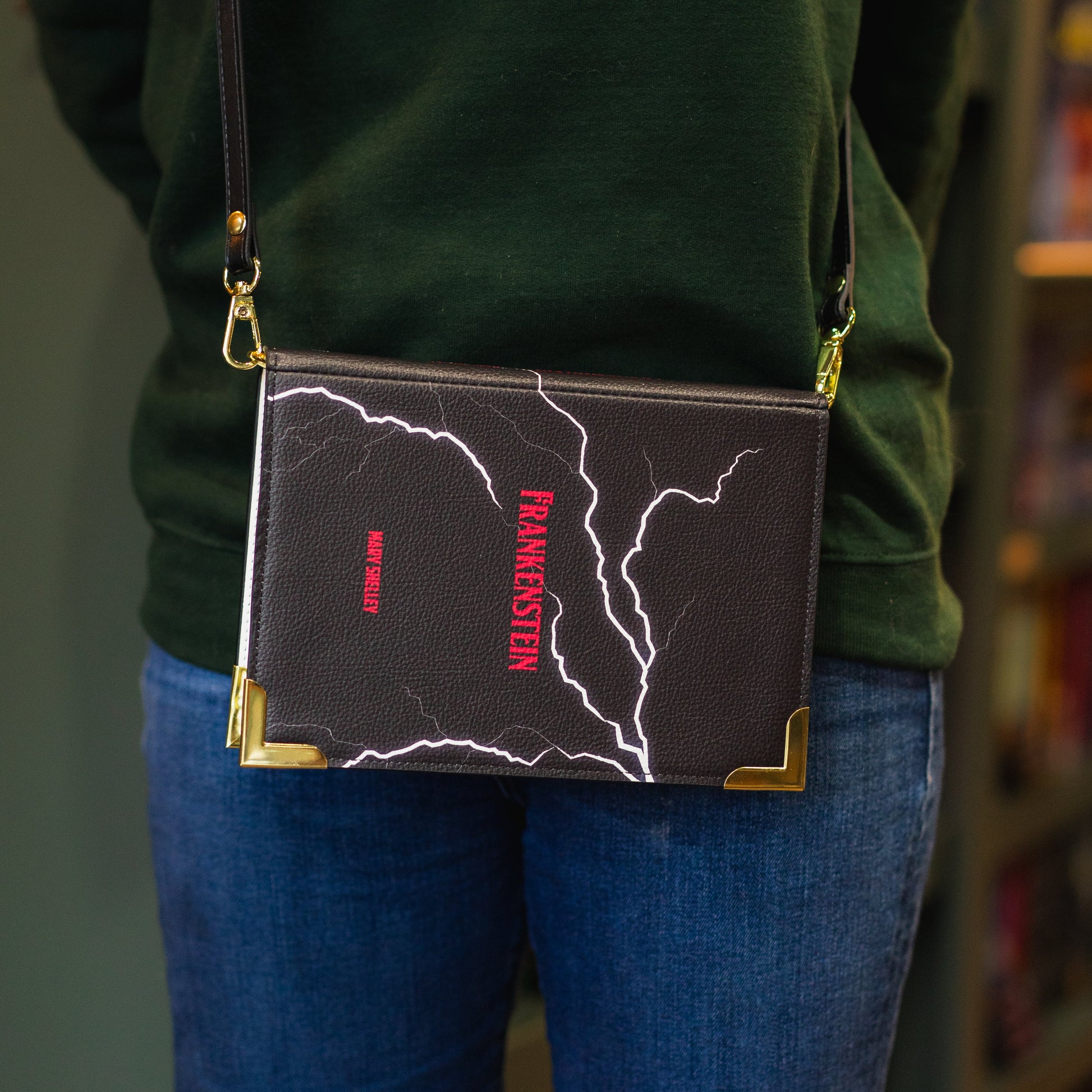 Person wearing a green sweater with 'The Archive' text, holding a black crossbody bag with red and white design.