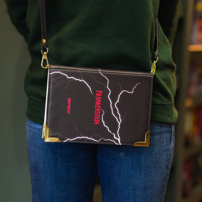 Person wearing a green sweater with 'The Archive' text, holding a black crossbody bag with red and white design.