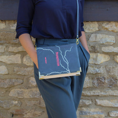 Person holding a book with 'Frankenstein' on the cover against a stone wall.