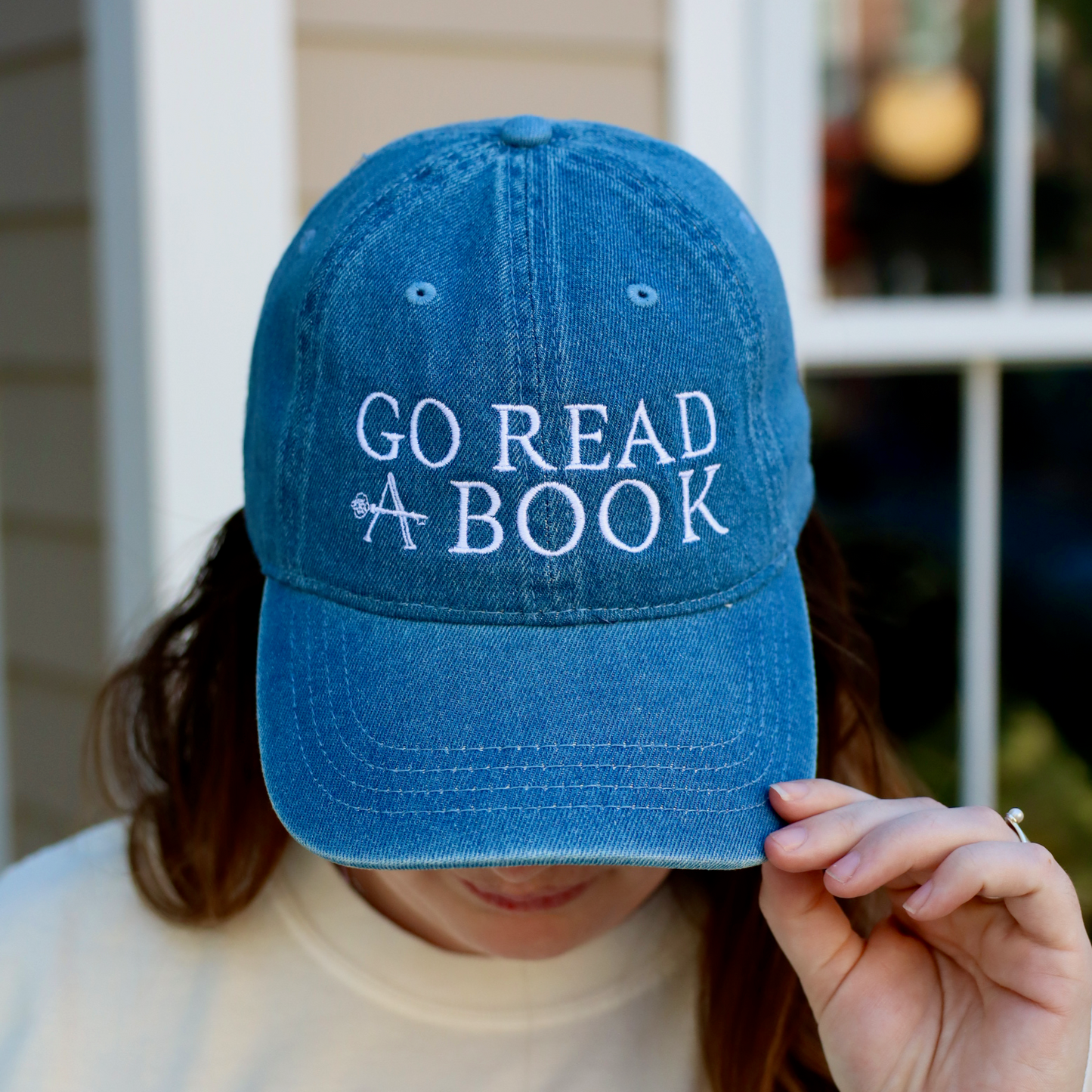 Person wearing a blue cap with 'GO READ A BOOK' text and a white t-shirt with 'SO DRAMATIC' text.
