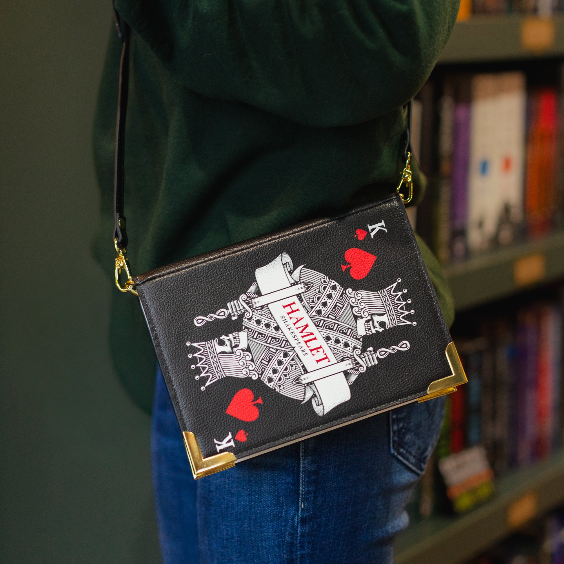 Person holding a black clutch with 'Hamlet' design in front of a bookshelf.