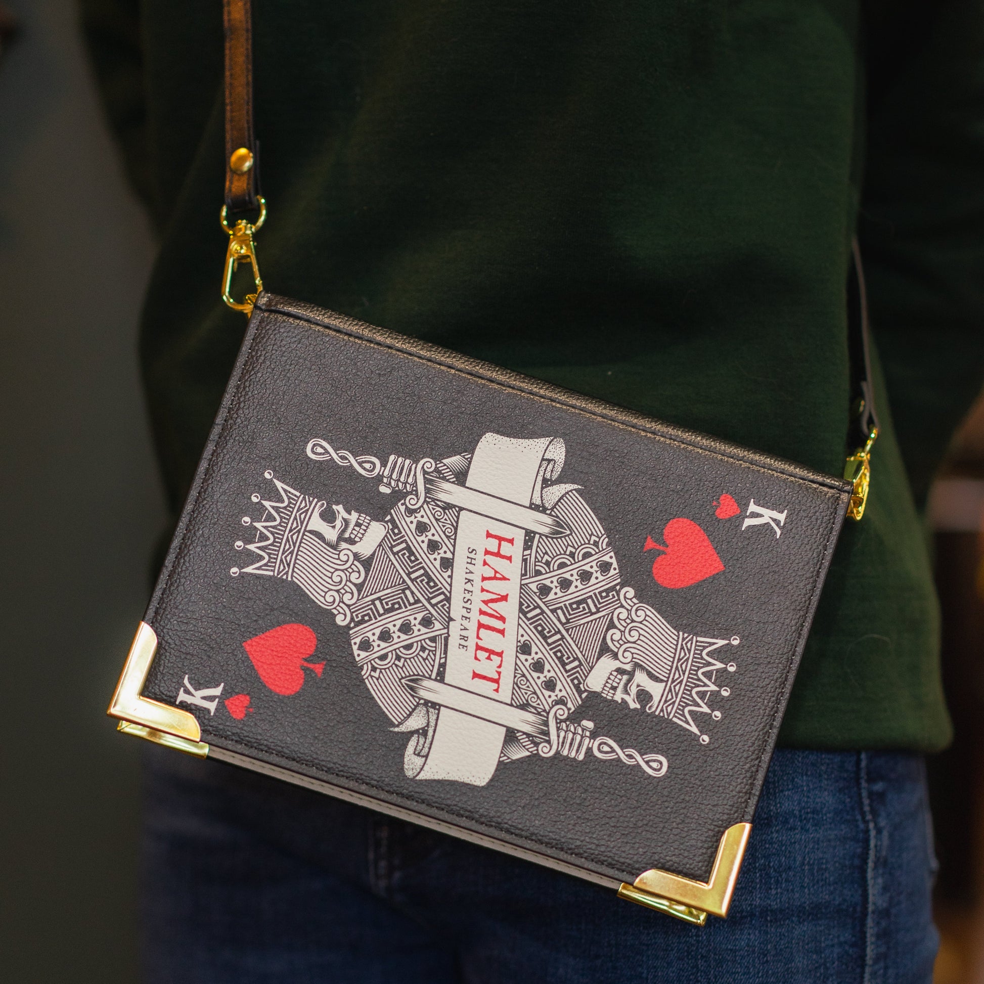 Handbag with playing card design held by a person wearing a green jacket.