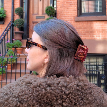 Person with gray hair wearing sunglasses and a fur-lined coat in front of a brick building.
