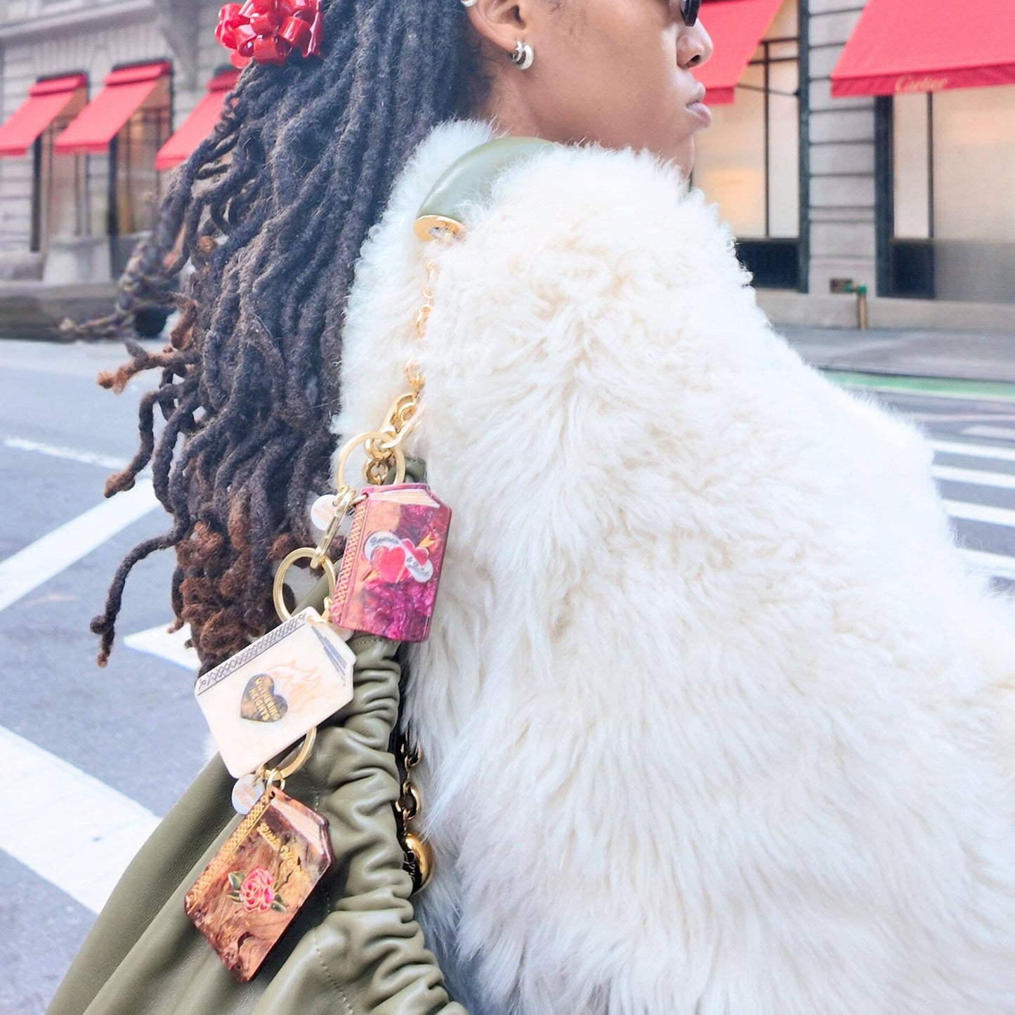 Person with braided hair wearing Hand-painted Wuthering Heights Book Bag Charm + Keychain and a white fur coat on a city street.