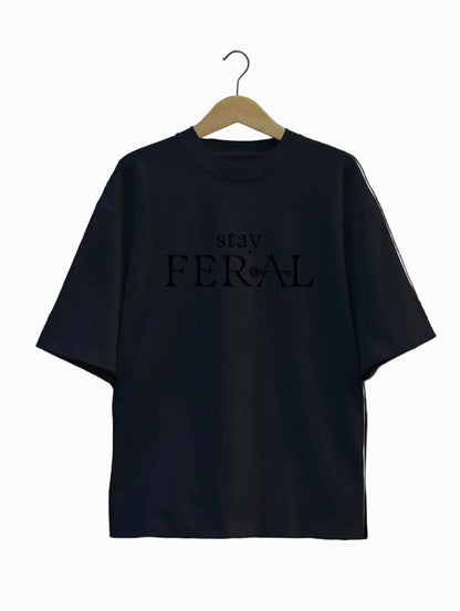 Black t-shirt with 'stay FERAL' text on a hanger against a light gray background