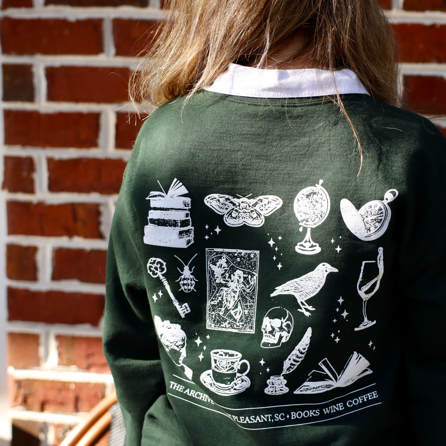 Person wearing a green sweatshirt with white graphics and text against a brick wall.