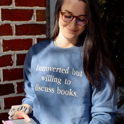 Woman wearing a blue sweatshirt with text, holding a book against a brick wall.