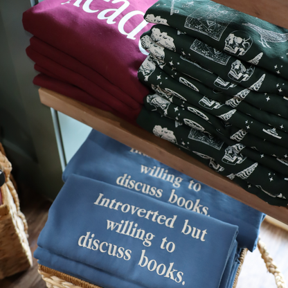 Stacks of t-shirts with text and graphics on a wooden shelf.