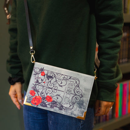 Person wearing a green hoodie with 'The Archive' logo, holding a gray clutch with red floral design.
