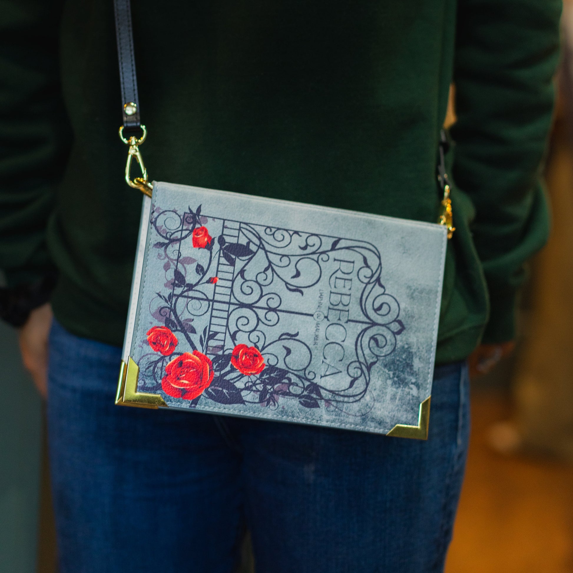 Person wearing a green sweater with a decorative bag featuring red flowers and intricate designs.