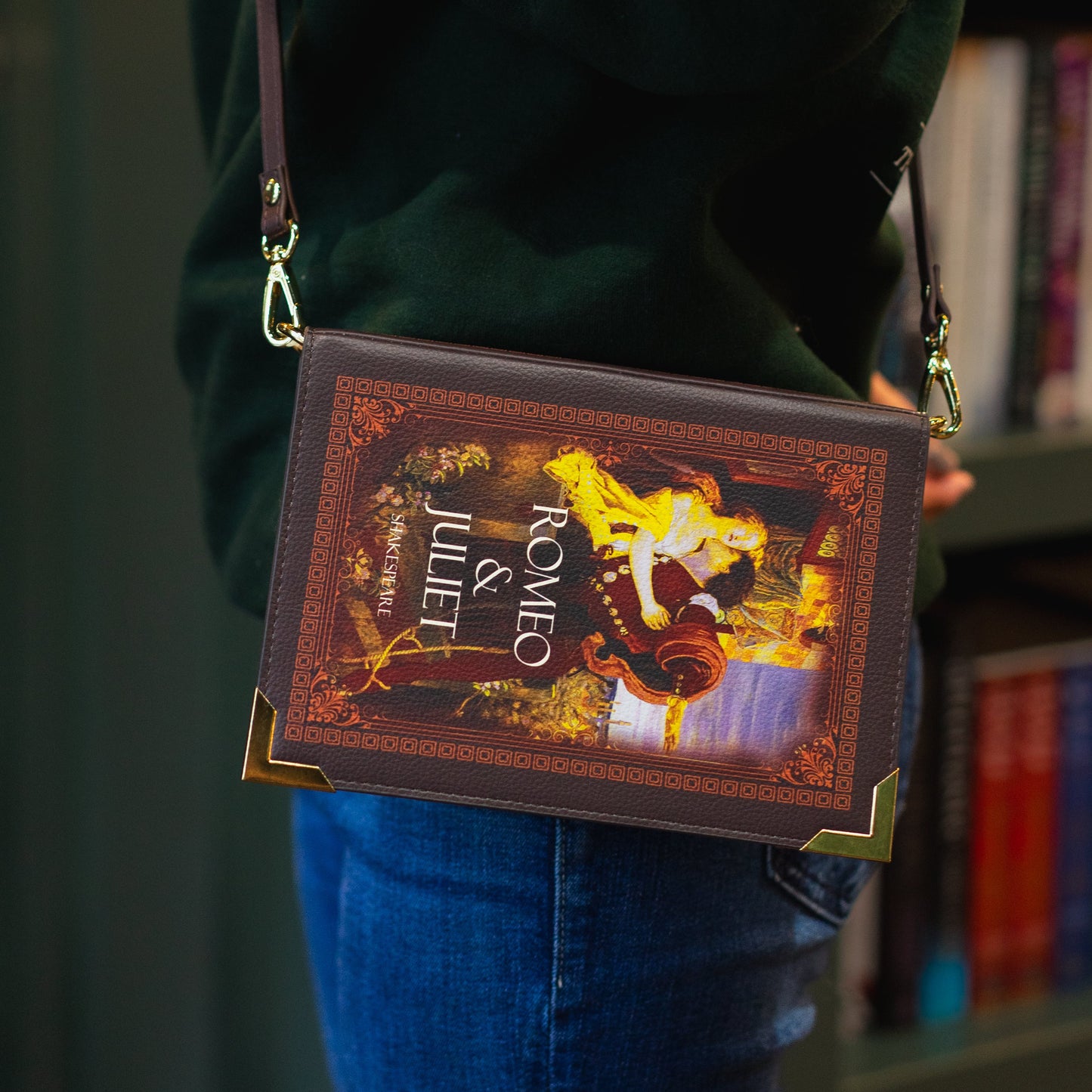 Person holding a book-themed handbag with 'Romeo and Juliet' design against a bookshelf background