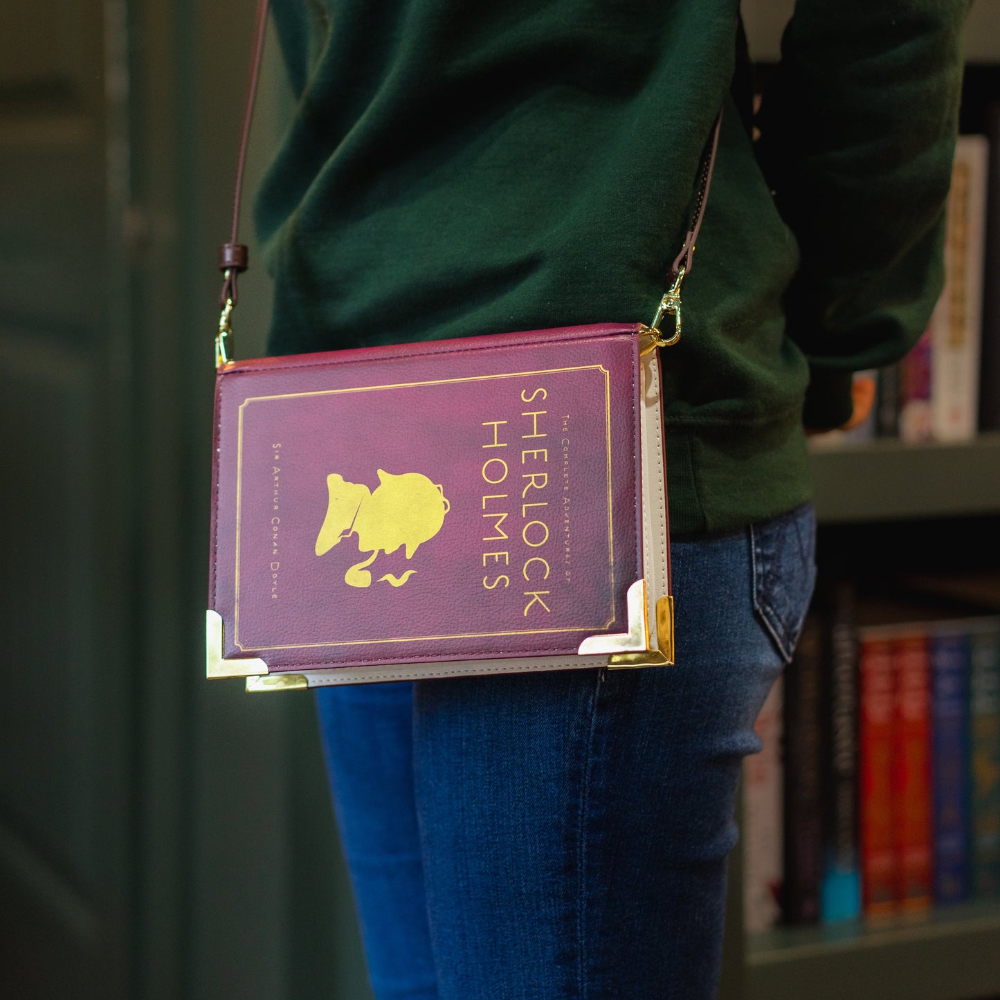 Person wearing a green hoodie with 'The Archive' logo, holding a purple book-shaped bag.
