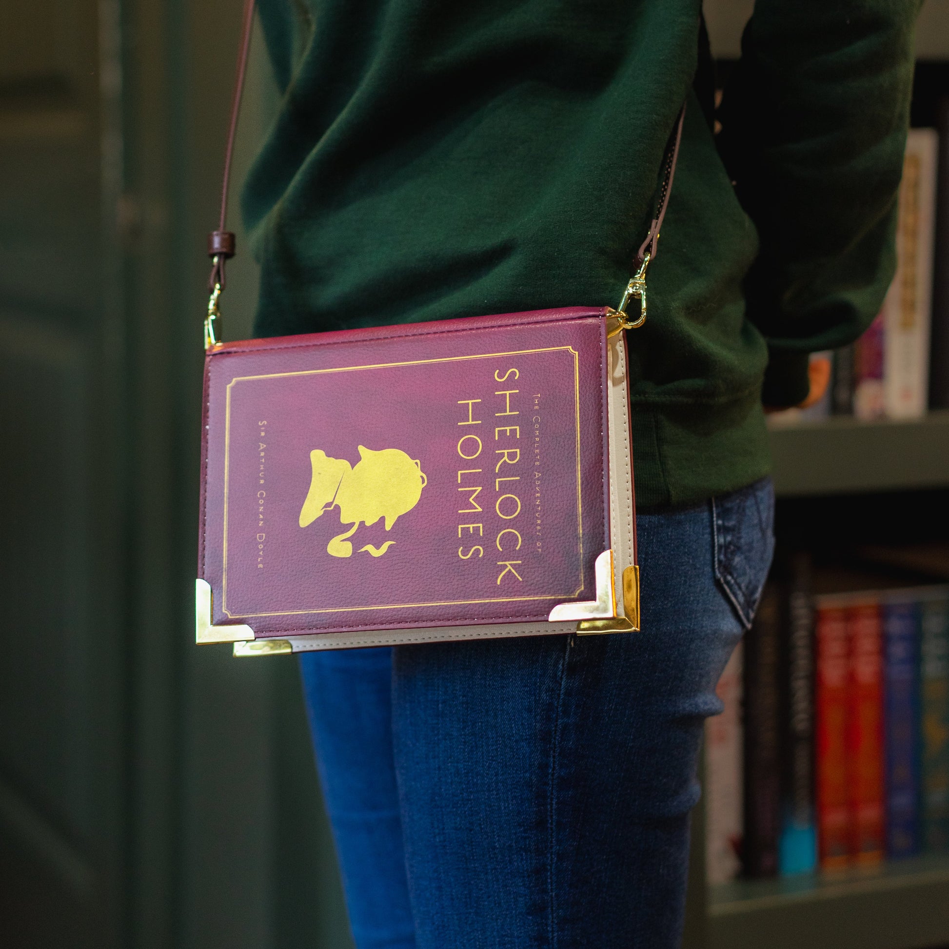 Person wearing a green hoodie with 'The Archive' logo, holding a purple book-shaped bag.