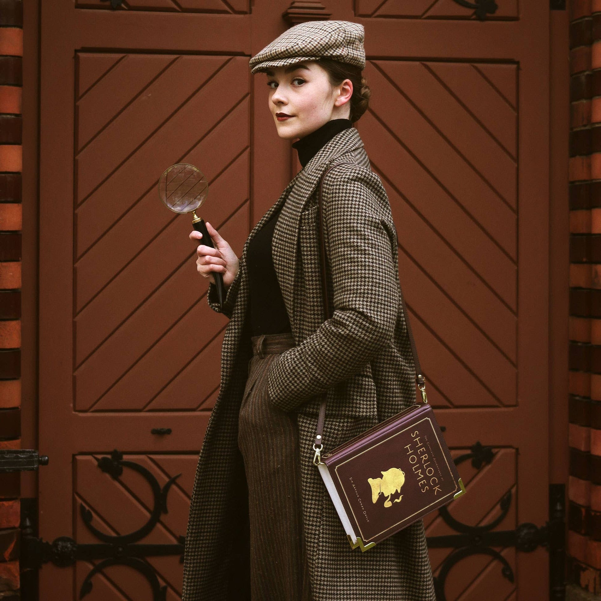 Woman in vintage attire with a magnifying glass and book against a brown door background