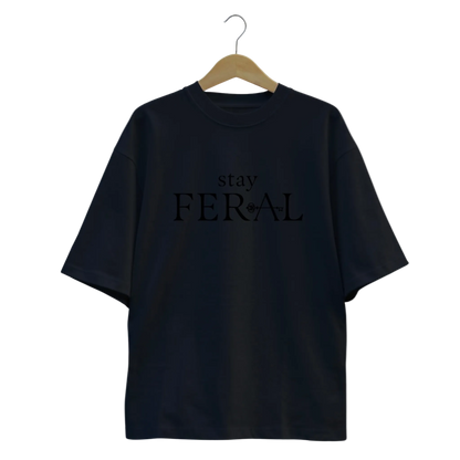 Black t-shirt with 'stay FERAL' text on a hanger against a white background
