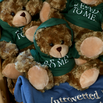 Stuffed teddy bears wearing green hoodies with text, sitting on a blue surface.