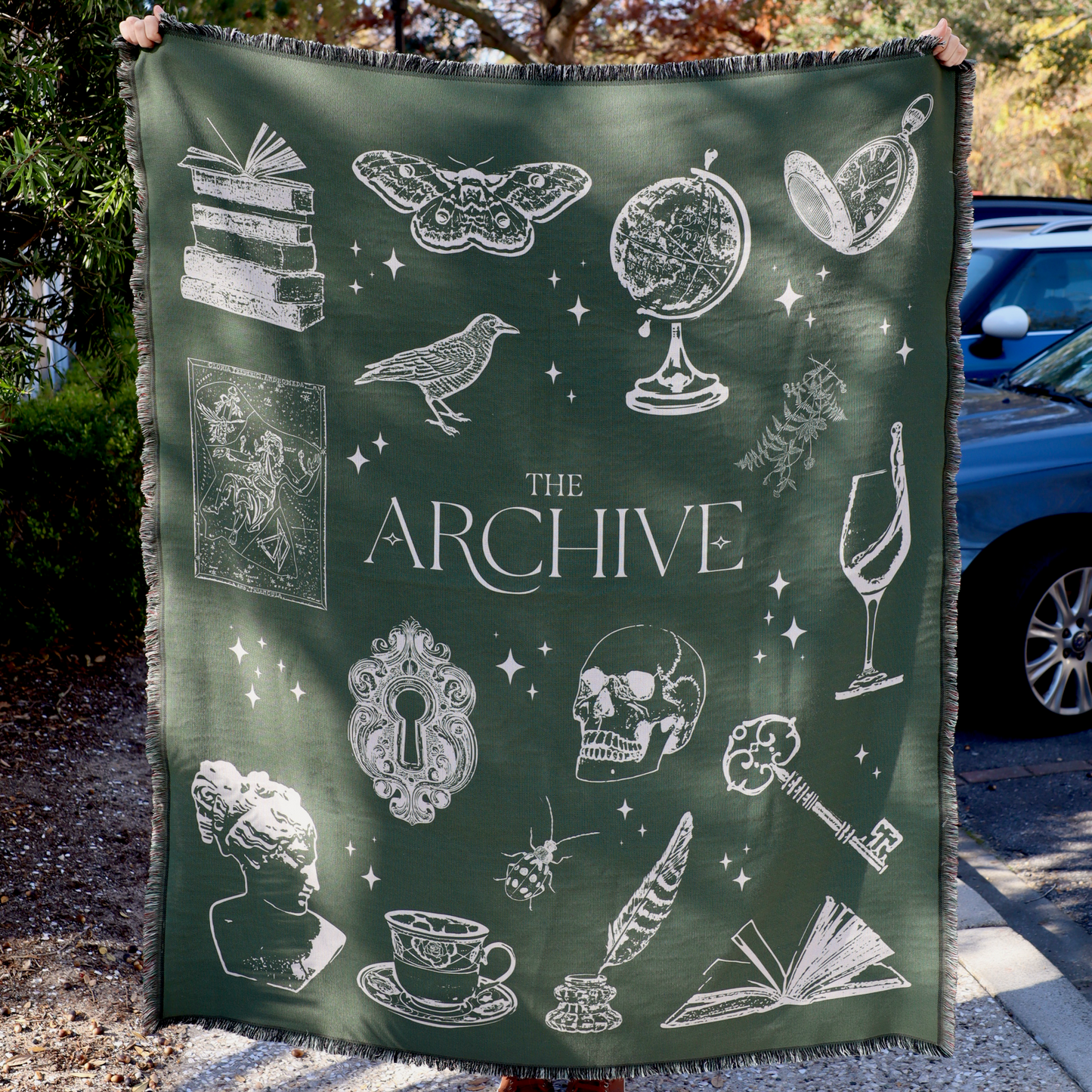 Person holding a green blanket with white illustrations and 'The Archive' text.