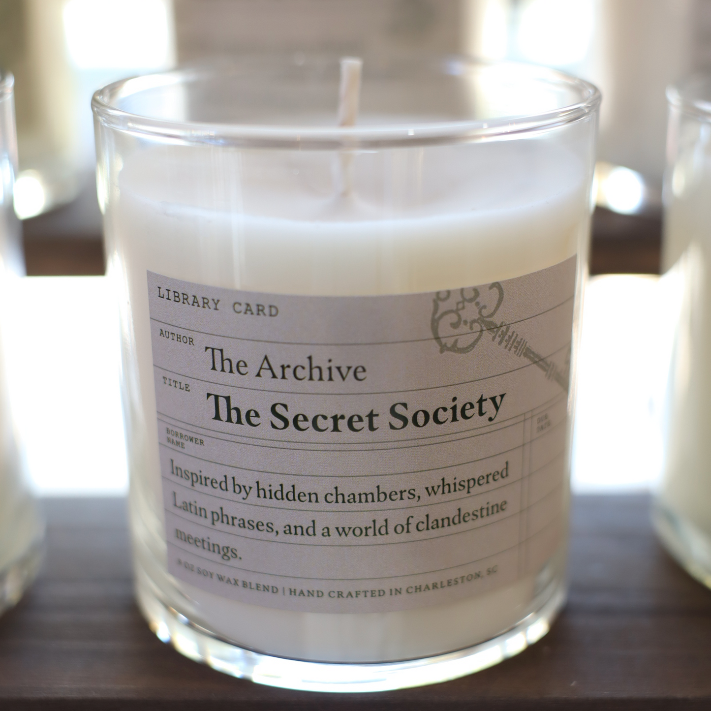 Candle in a glass jar with a label titled 'The Secret Society' on a wooden surface.