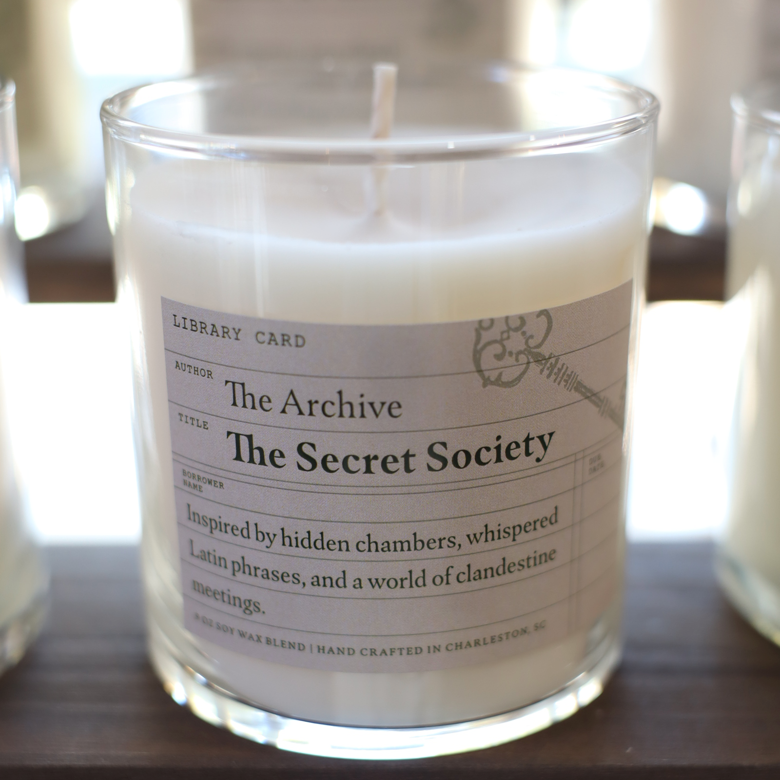 Candle in a glass jar with a label titled 'The Secret Society' on a wooden surface.