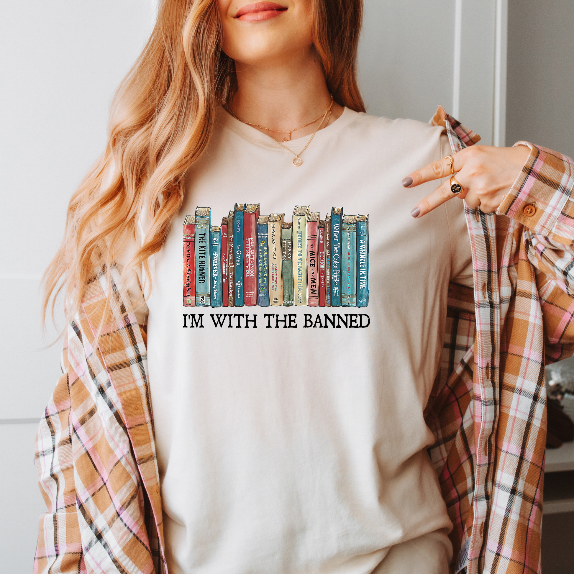 A person wearing a beige t-shirt with the text 'I'M WITH THE BANNED' and a graphic of a row of various books.