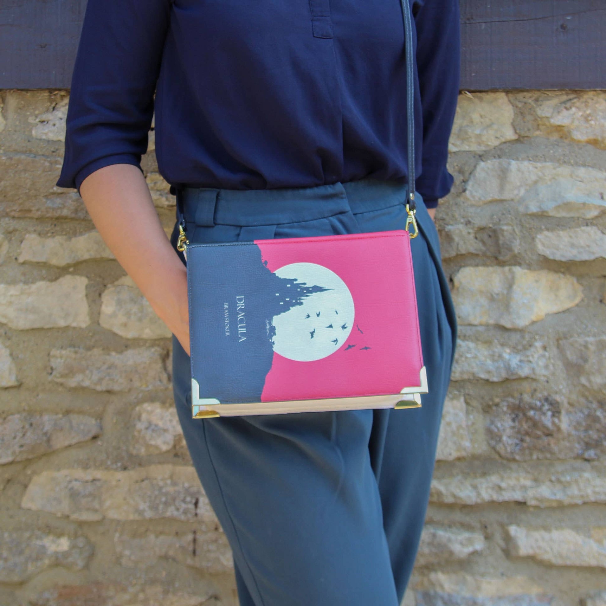 Person holding a book with a pink and blue cover against a stone wall.