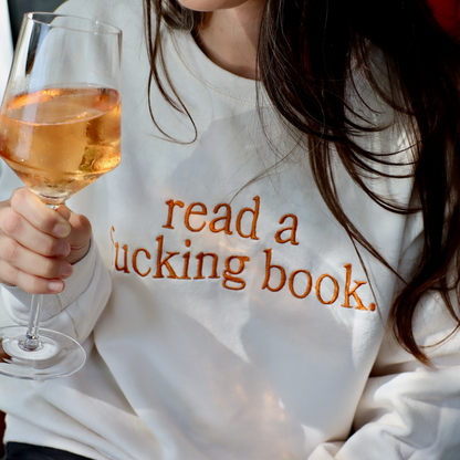 Person wearing a white sweatshirt with text holding a glass of wine.